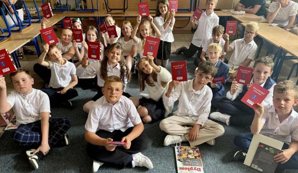 Dzieci siedzą z Paszportami Sportowymi w rękach